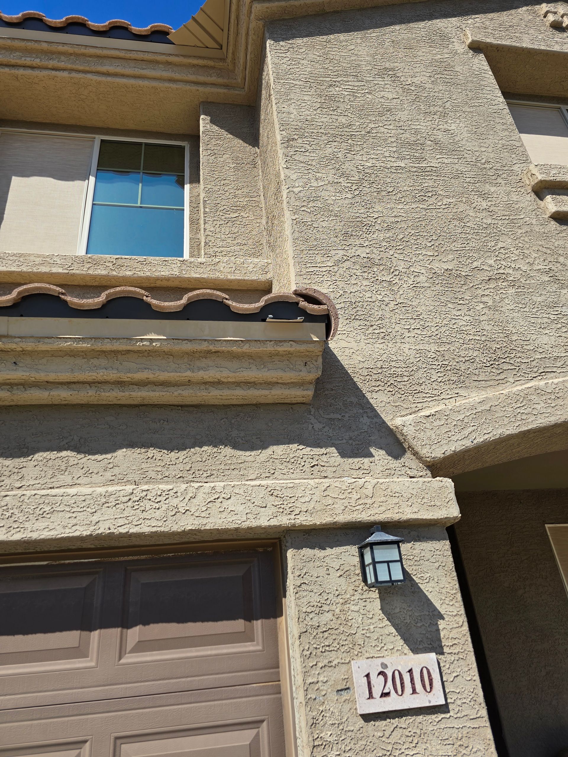 Tan stucco house exterior with a window, garage door, and address 12010.