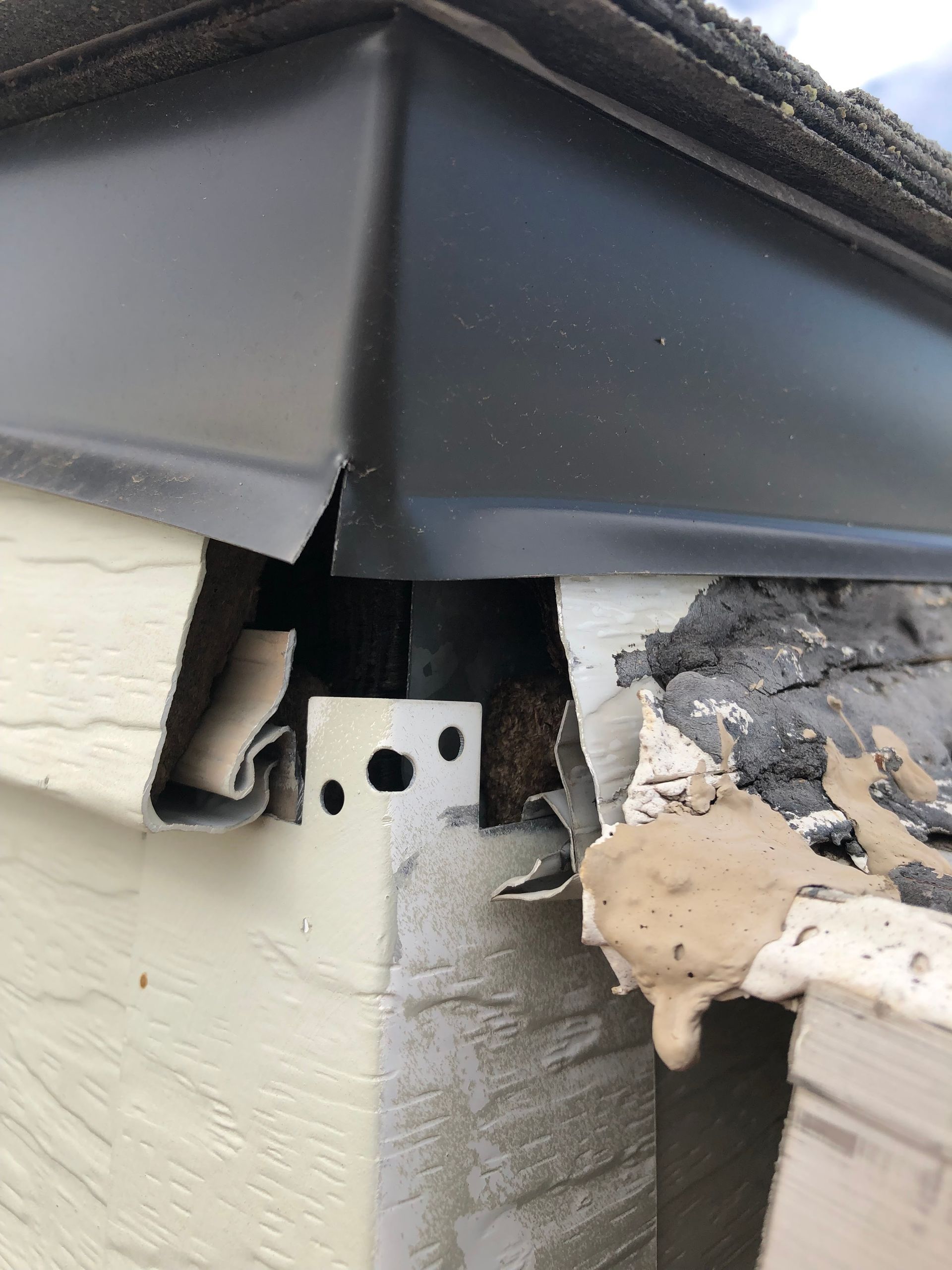 Close-up of a damaged corner of a building with black flashing and exposed structural components.