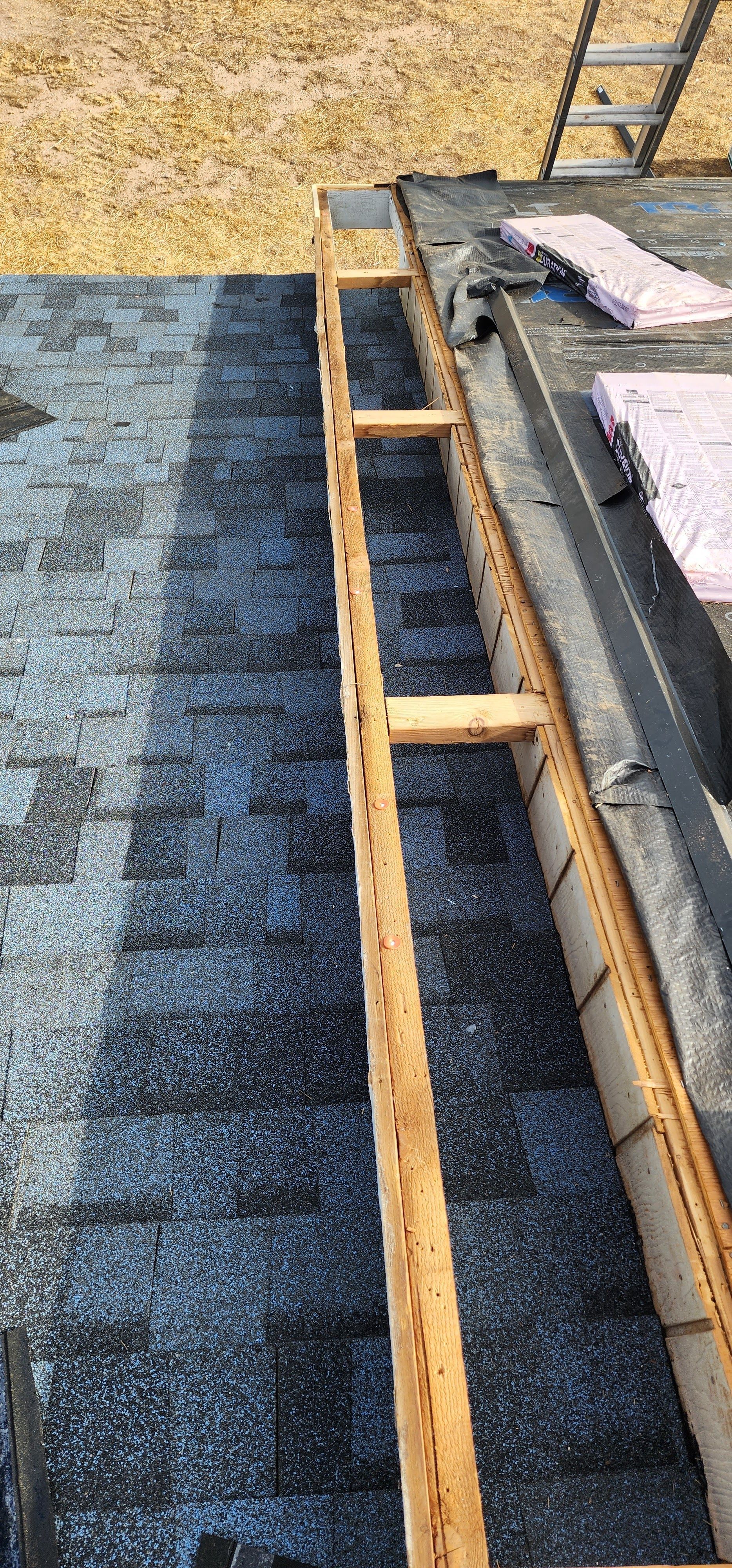 A long wooden frame on a black rooftop, possibly for roofing work. A ladder and insulation are also visible.