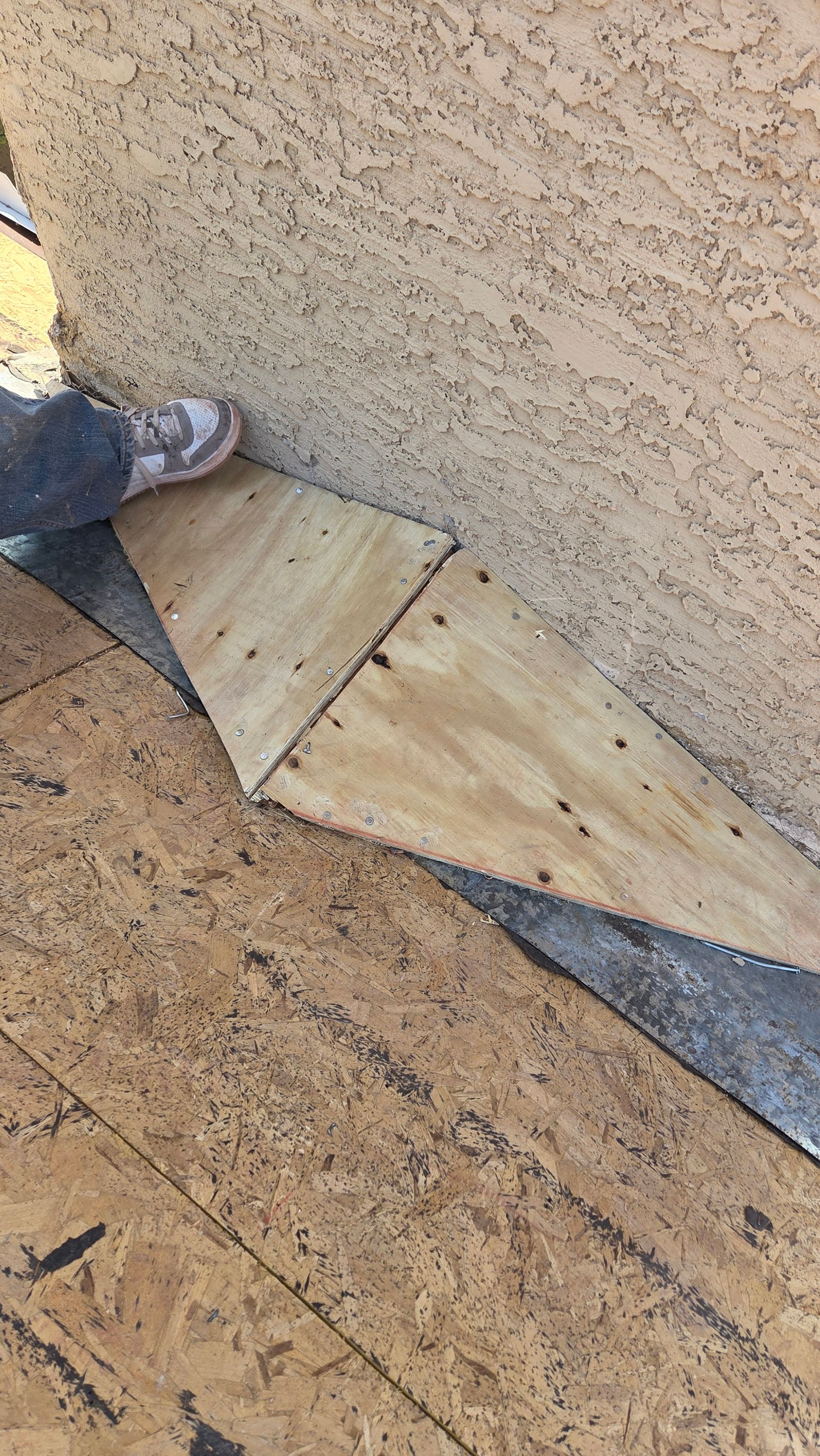 Person standing on a roof with plywood pieces and roofing material.