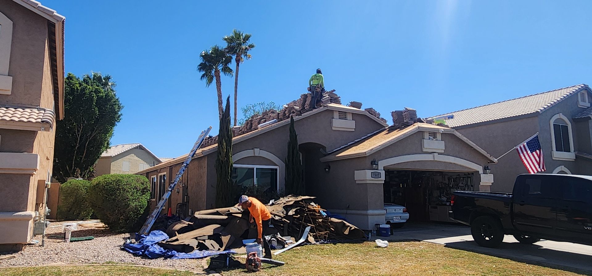 Roofers working on a house under a sunny sky. Debris and tools are visible.