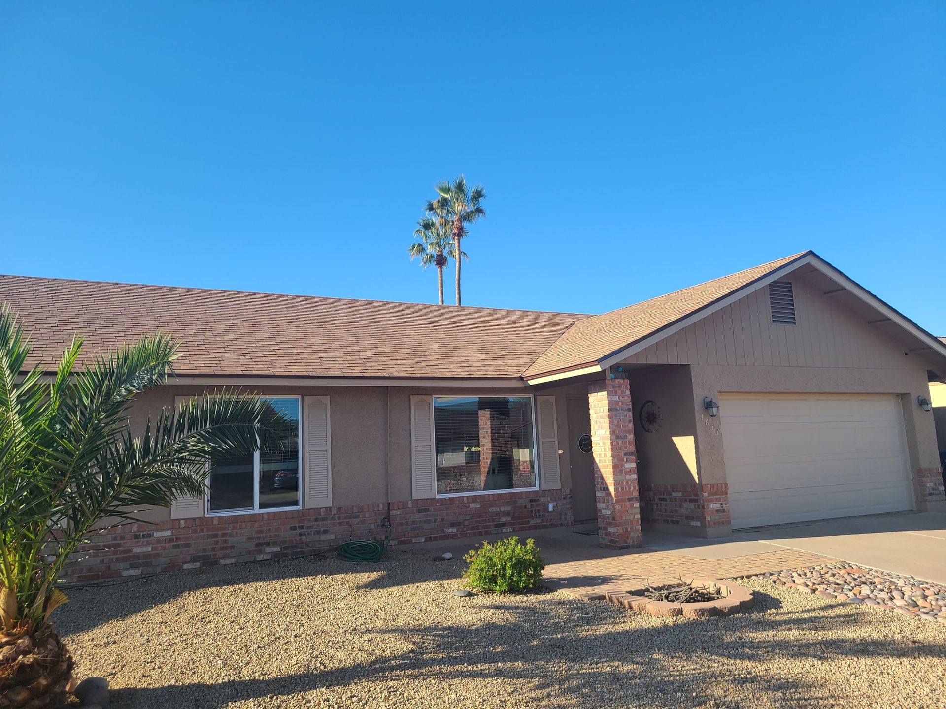 Beige suburban house with brown roof and palm trees against a clear blue sky.
