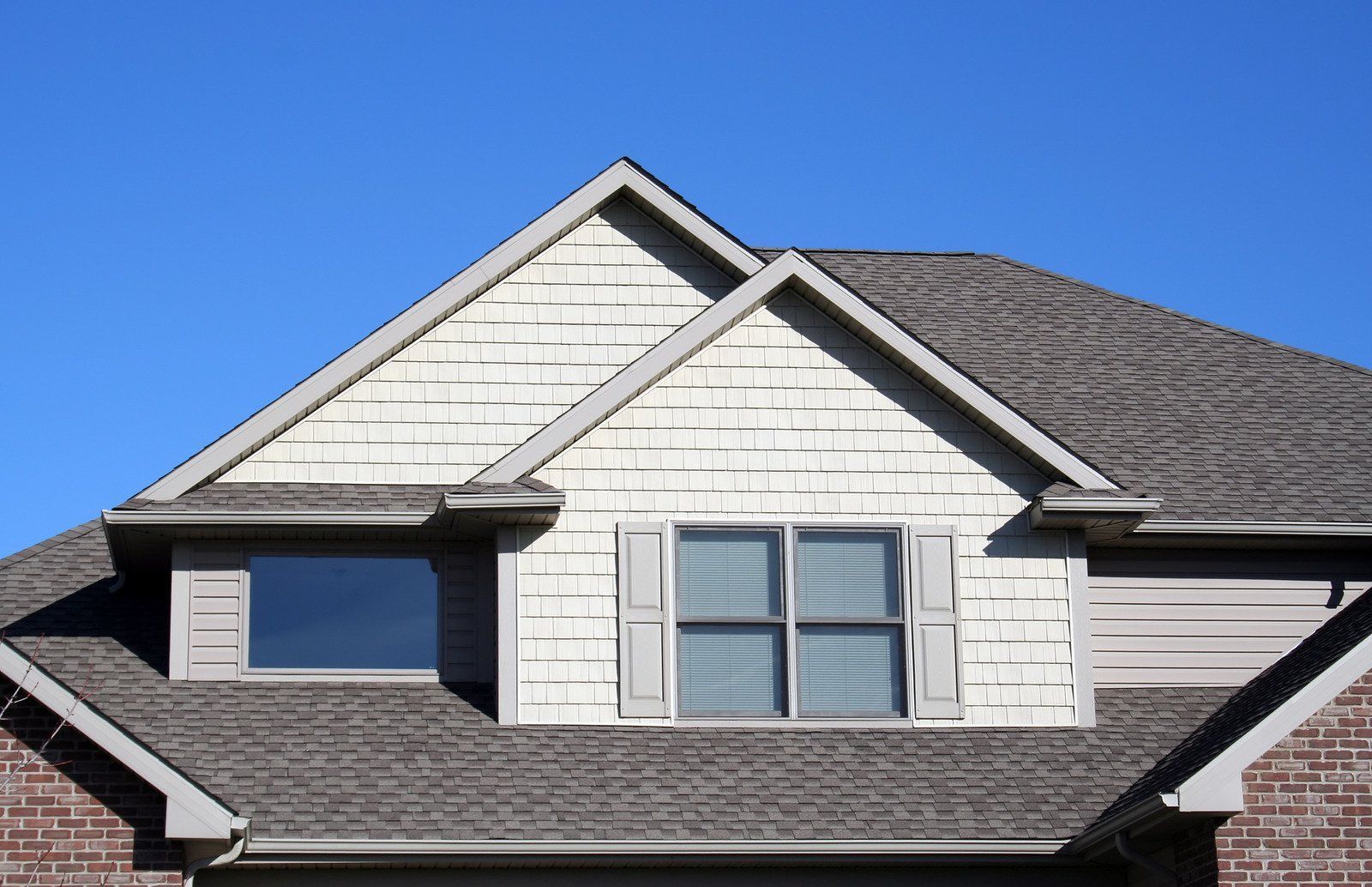 Close-up of a house roof with two dormers. The sky is blue.