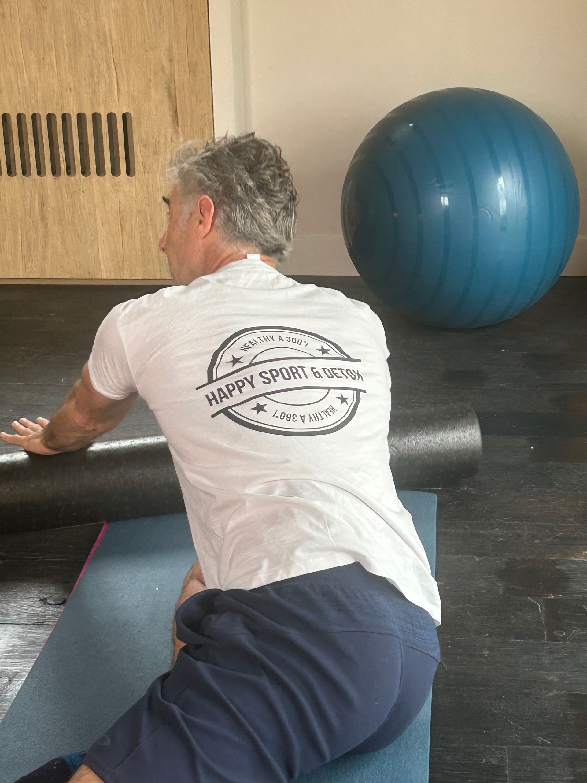 Un homme est assis sur un tapis de yoga avec une balle bleue en arrière-plan.
