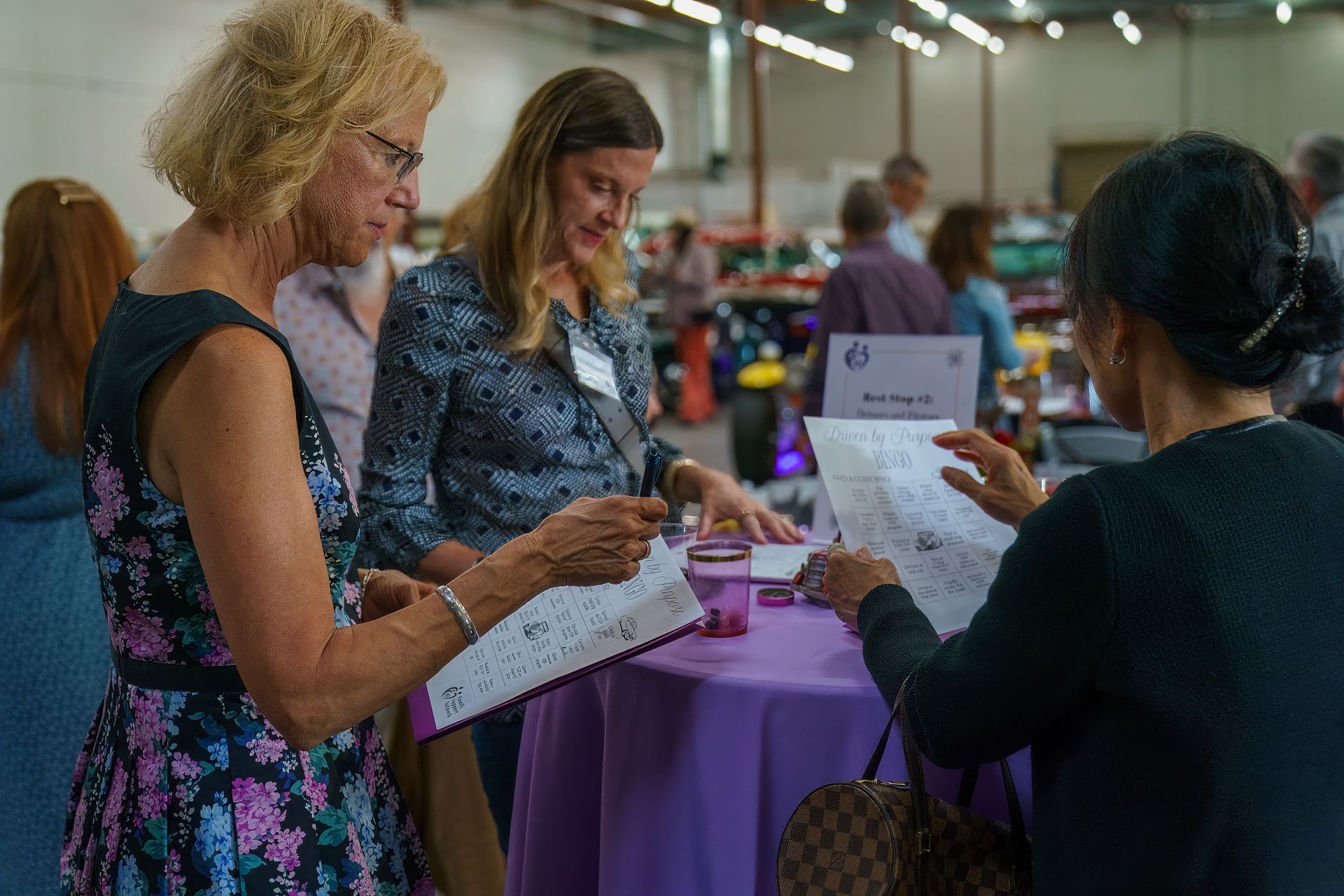 People signing in at a table with a purple tablecloth at an indoor event, with a staff member assisting.