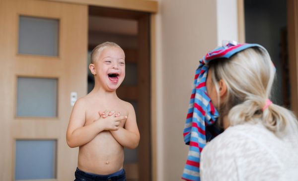 Smiling child at a doorway with shirt lifted, facing an adult in a striped headscarf