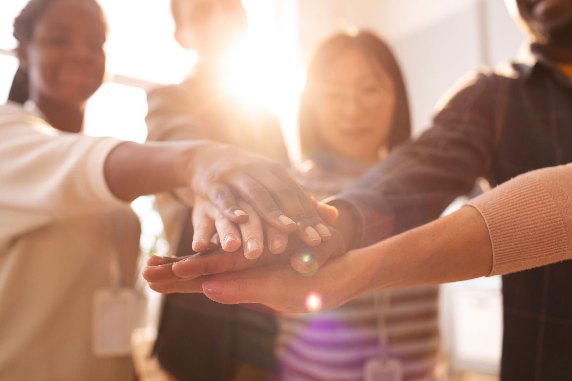 Hands stacked together in a bright outdoor team huddle with sunlight shining through.