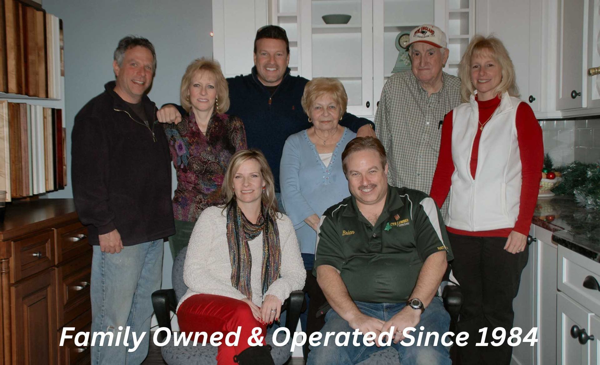 A group of nine people, smiling, standing and sitting in a kitchen, with the text