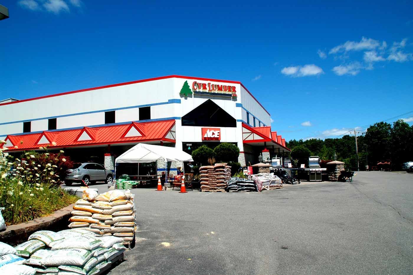 Exterior view of a home and garden store with red roof accents, outdoor displays, and parked vehicles on a sunny day.