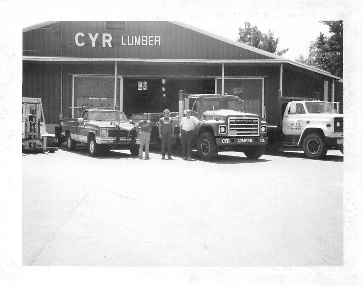 CYR Lumber building with three trucks and a forklift in front; four men pose near the trucks.
