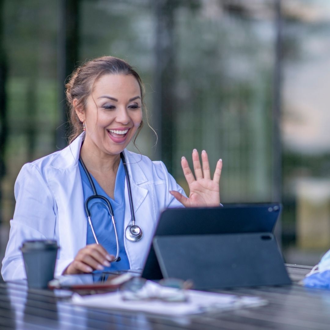 A female doctor is sitting at a table using a tablet computer.