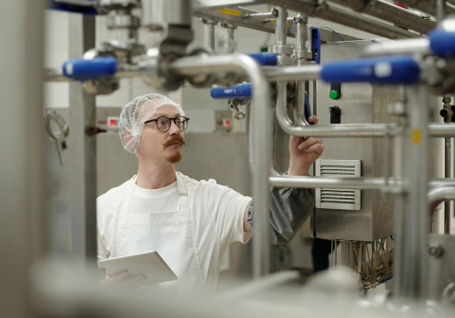 Worker in gloves monitoring a food production line filling metal containers.