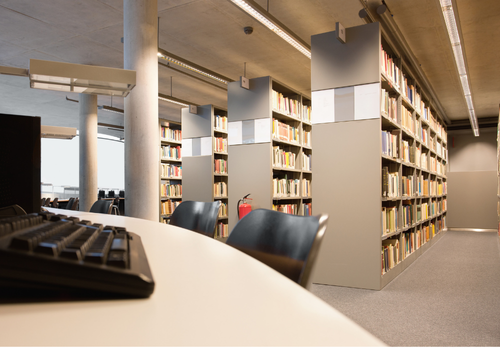 Library aisle with bookshelves and a computer workstation in the foreground.