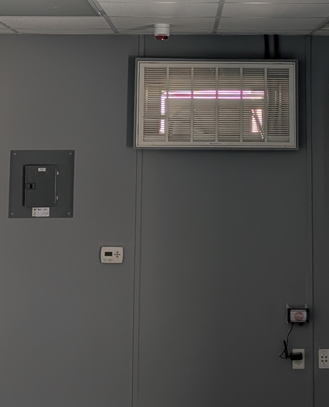 A large, gray electrical cabinet on a building exterior, covered in snow; a blue piece of equipment attached.