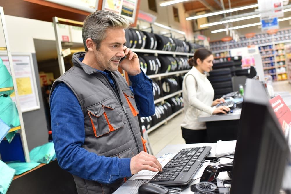 A Man is Talking on a Cell Phone While Using a Computer in a Store — Hancock Automotive in Bennetts Green, NSW
