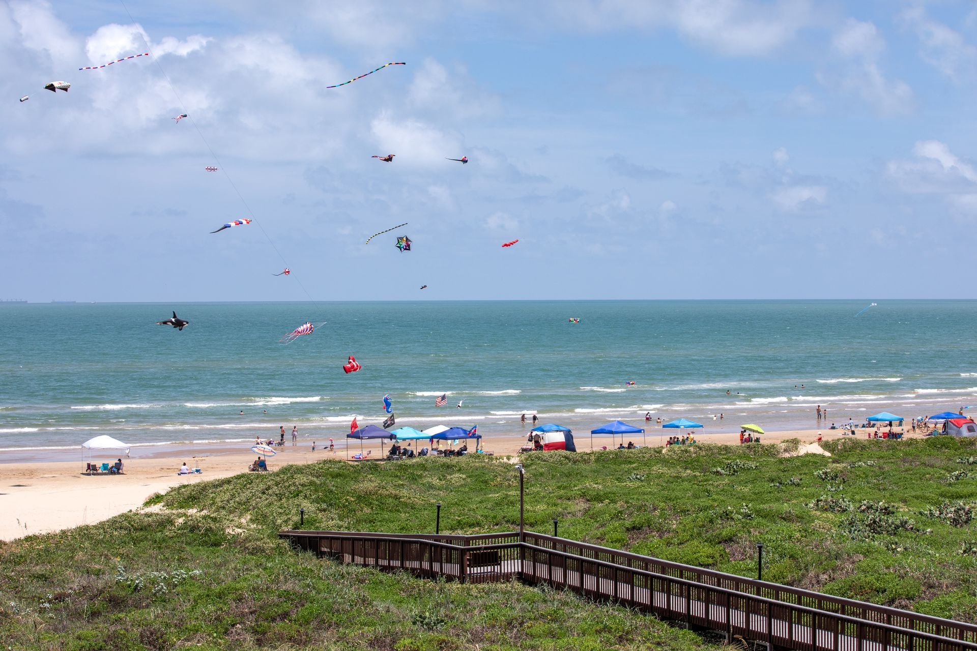 A boardwalk leading to a beach with kites flying in the sky