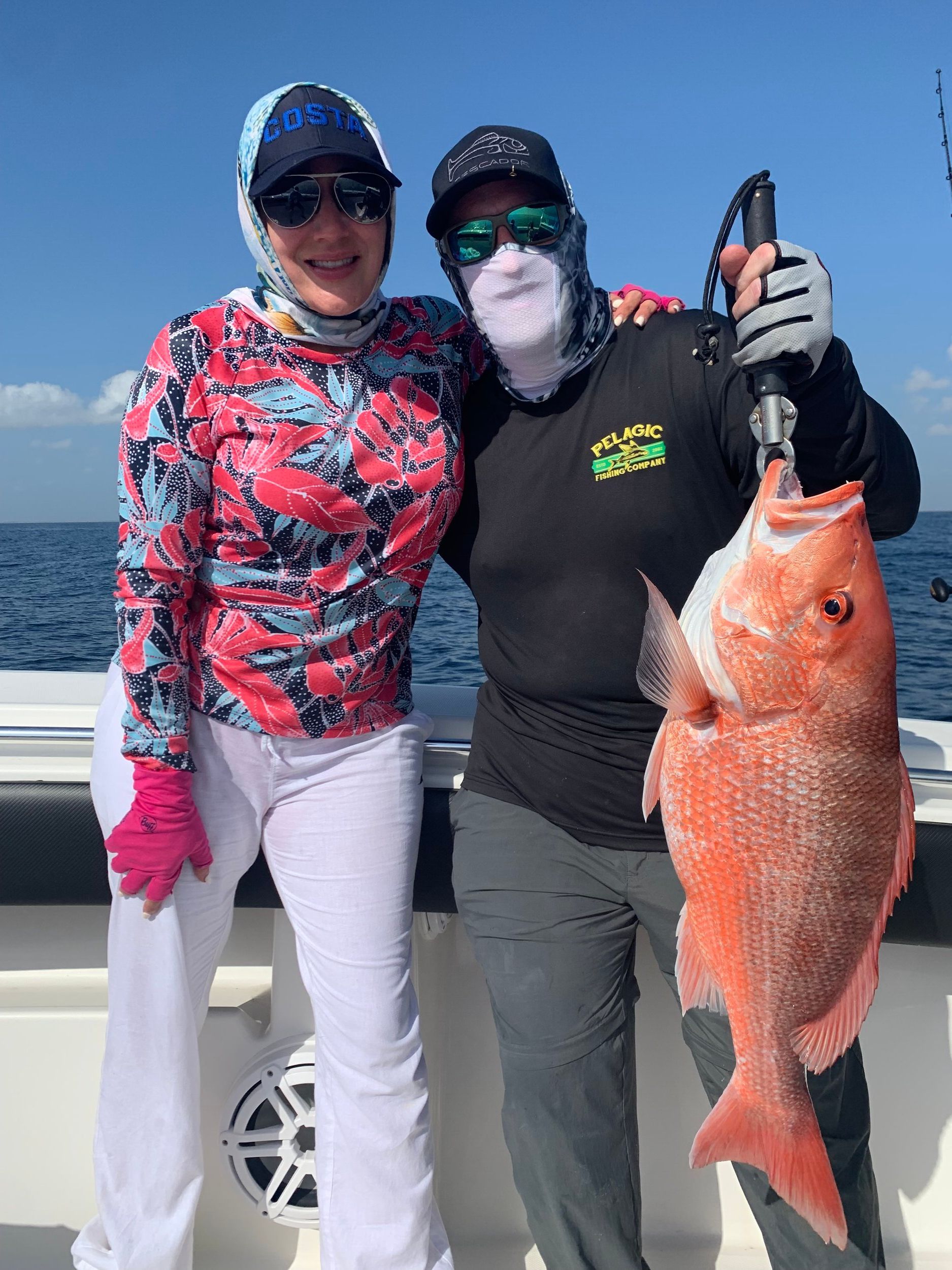 Two women are standing next to each other on a boat holding a large red fish.