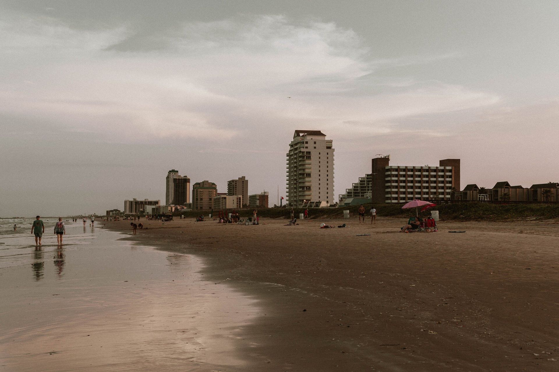 A beach with a city in the background and people walking on it