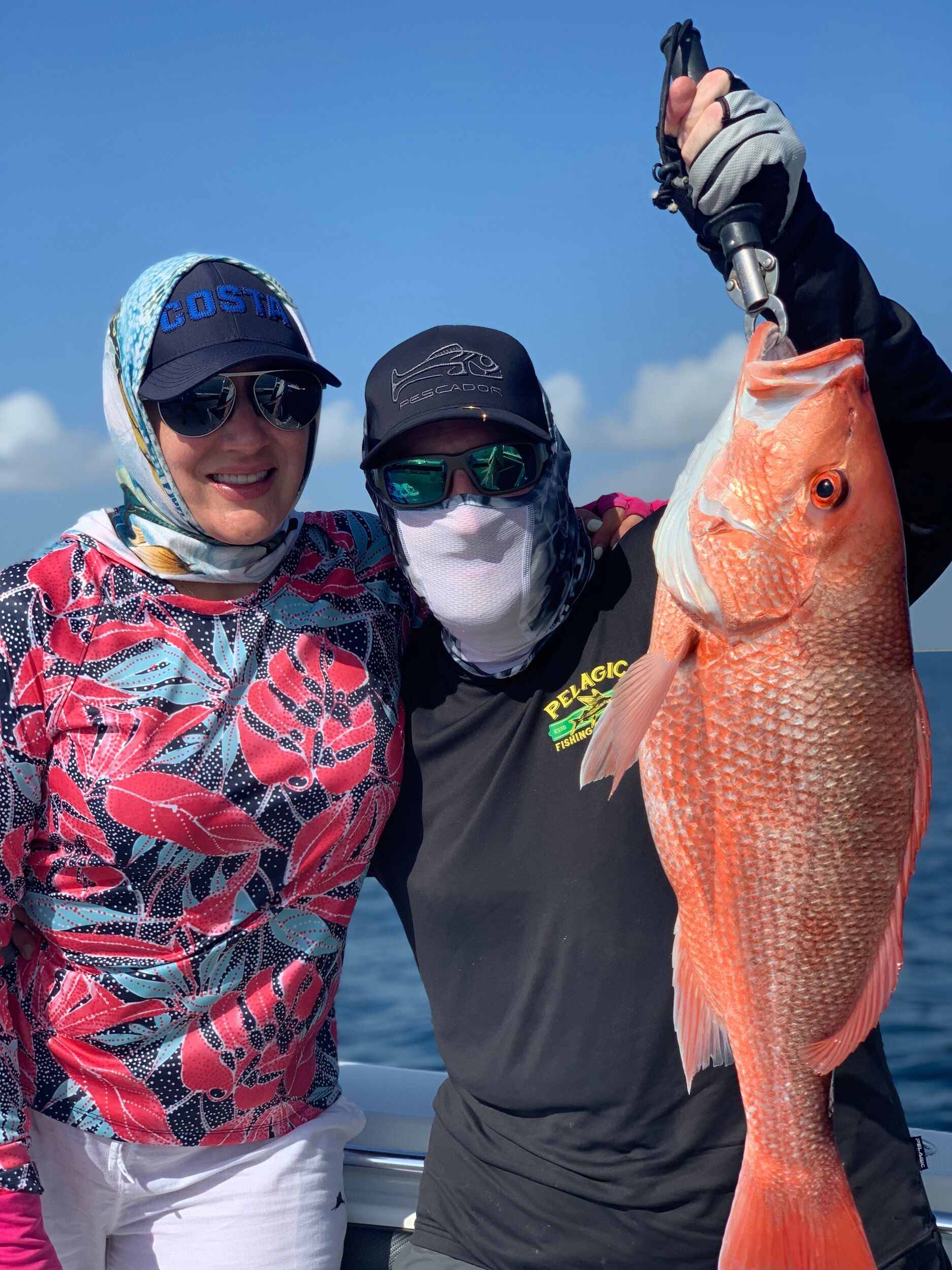 A man and a woman are holding a large red fish on a boat.