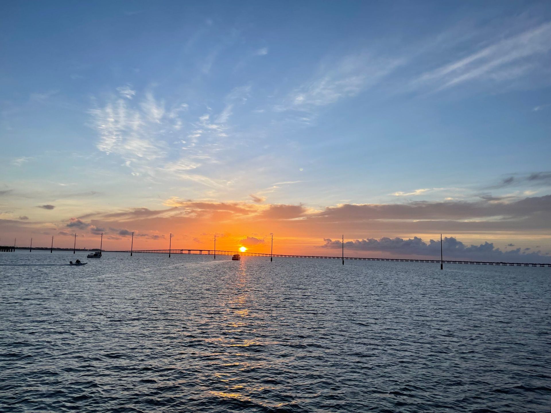 A sunset over a large body of water with a bridge in the distance.