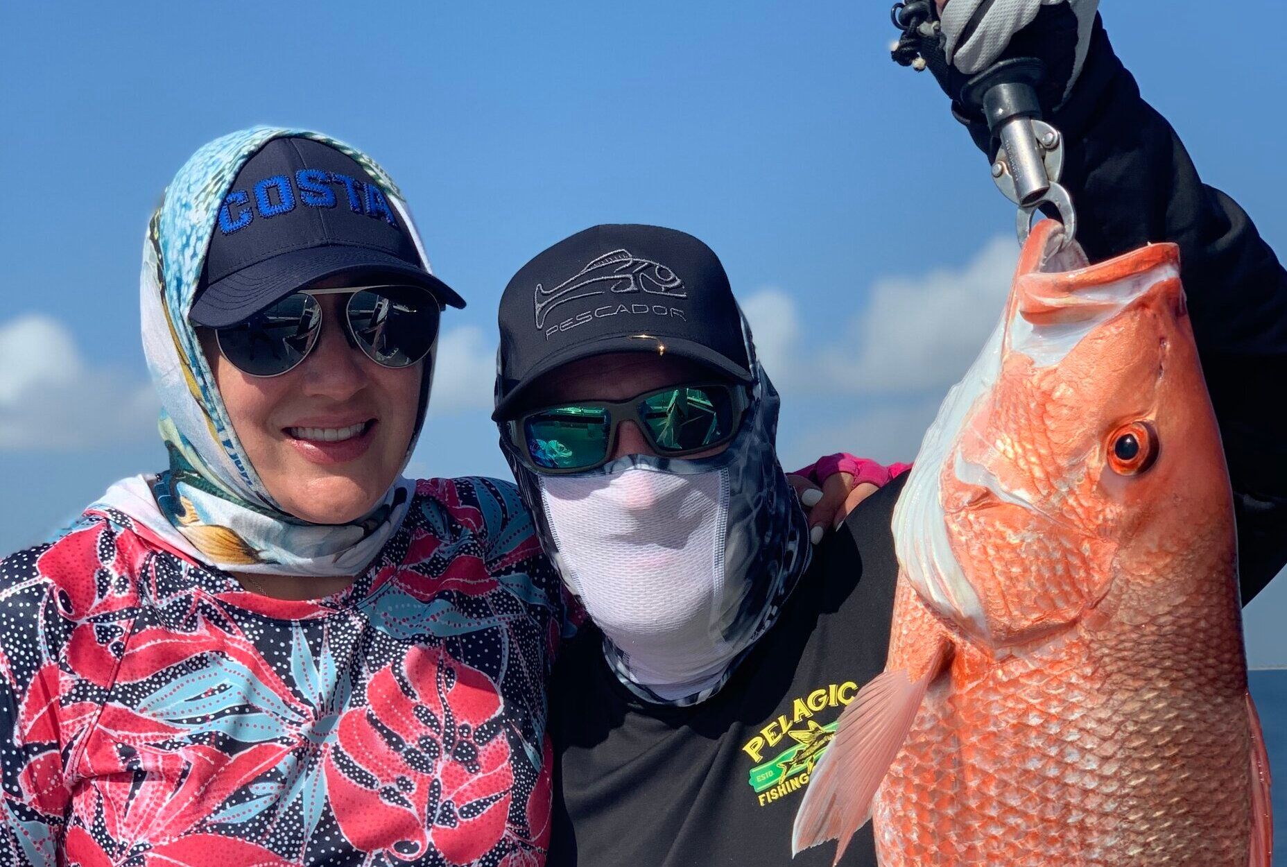 A man and a woman are standing next to each other holding a large red fish.