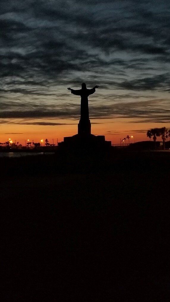 A statue of jesus is silhouetted against a sunset sky.