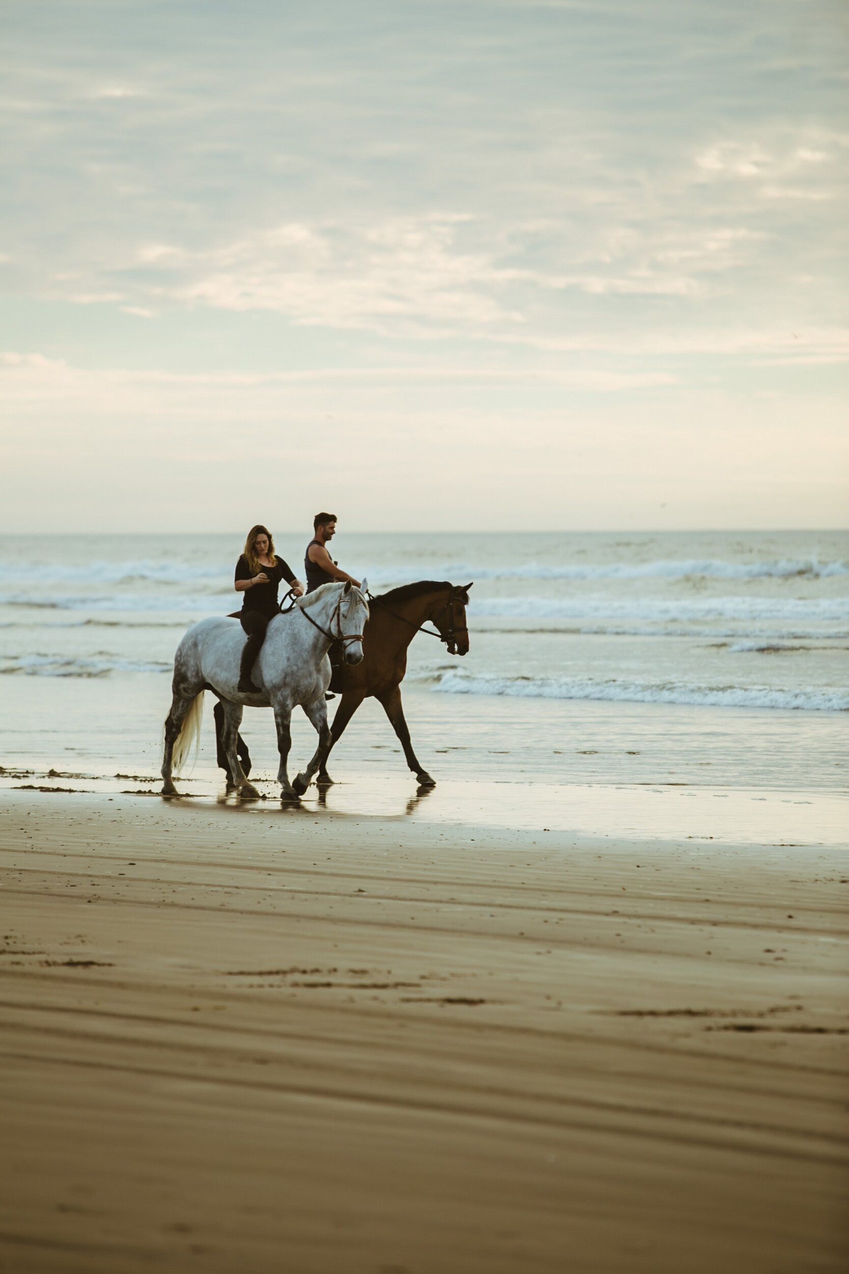 Two people are riding horses on the beach.