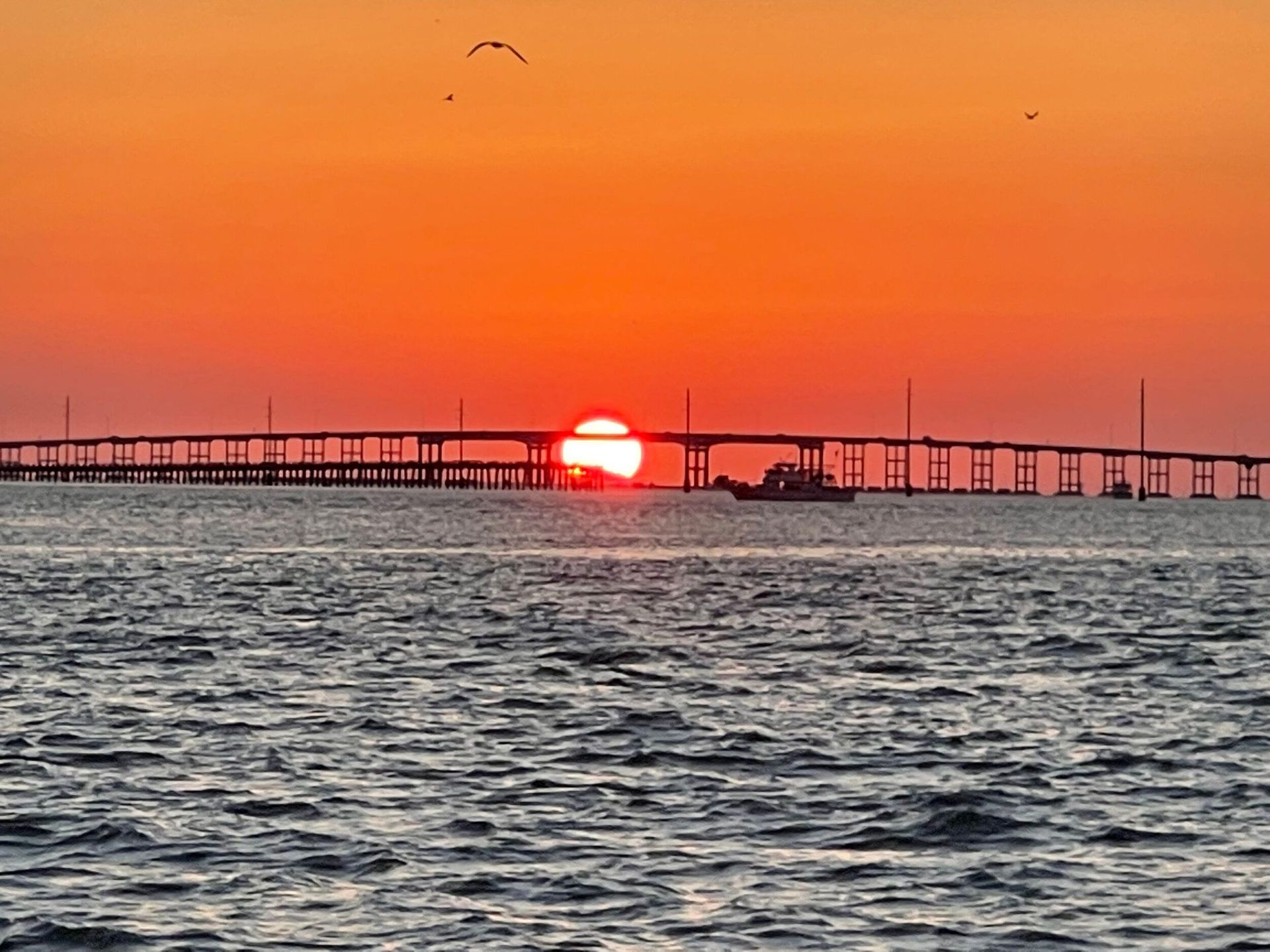 The sun is setting over a bridge over the ocean
