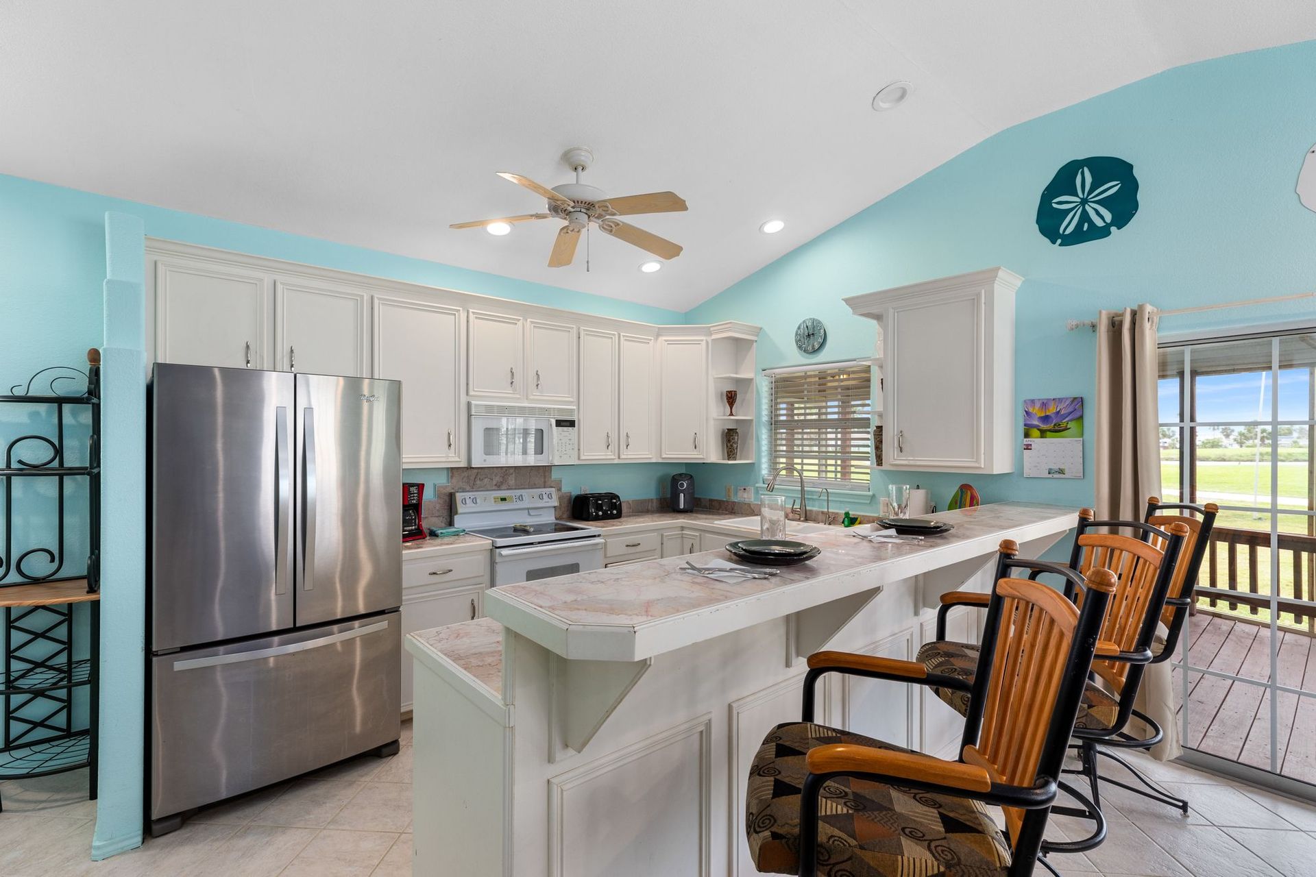 A kitchen with white cabinets , stainless steel appliances , a refrigerator and a bar.