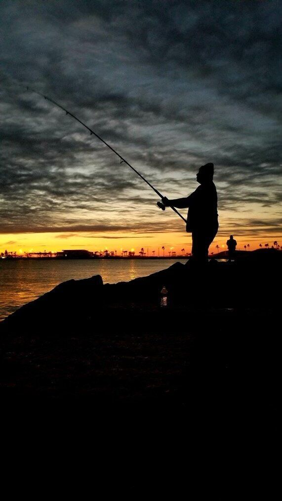 A man is fishing in the ocean at sunset.