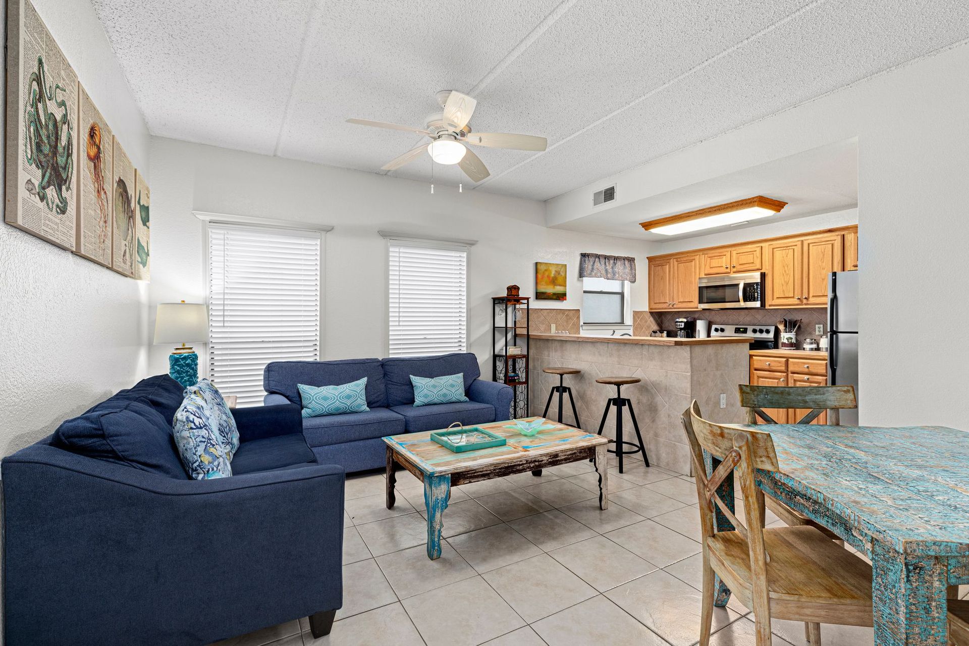 A living room with a blue couch , table , chairs and a ceiling fan.