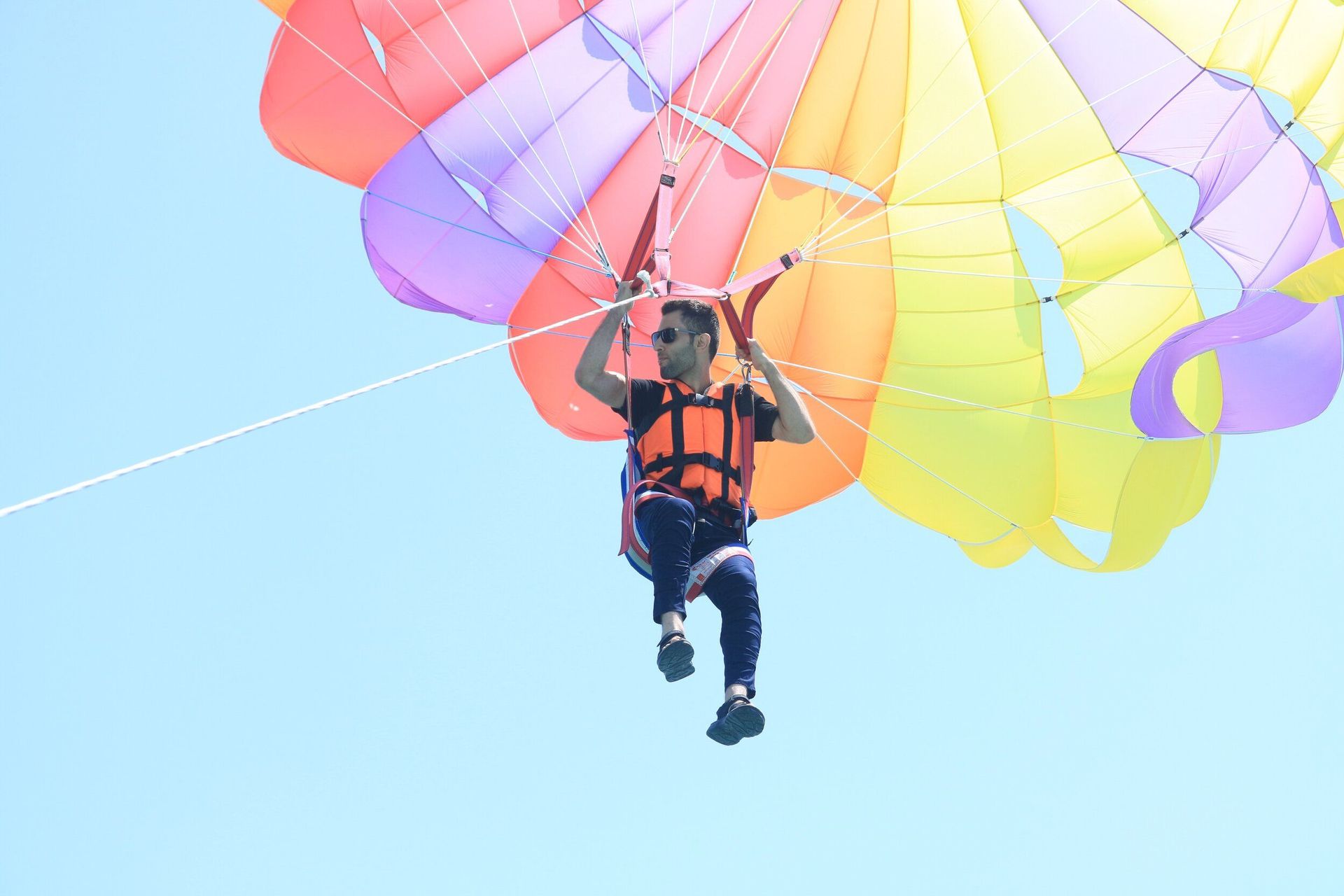 A man is flying through the air on a colorful parachute.