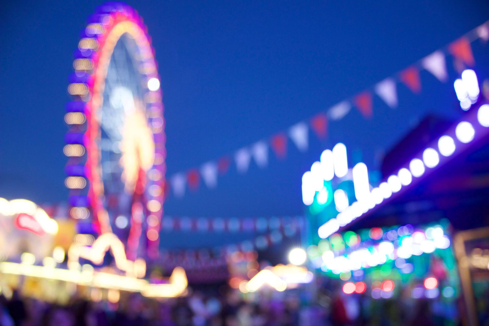 A blurry picture of a carnival with a ferris wheel in the background.