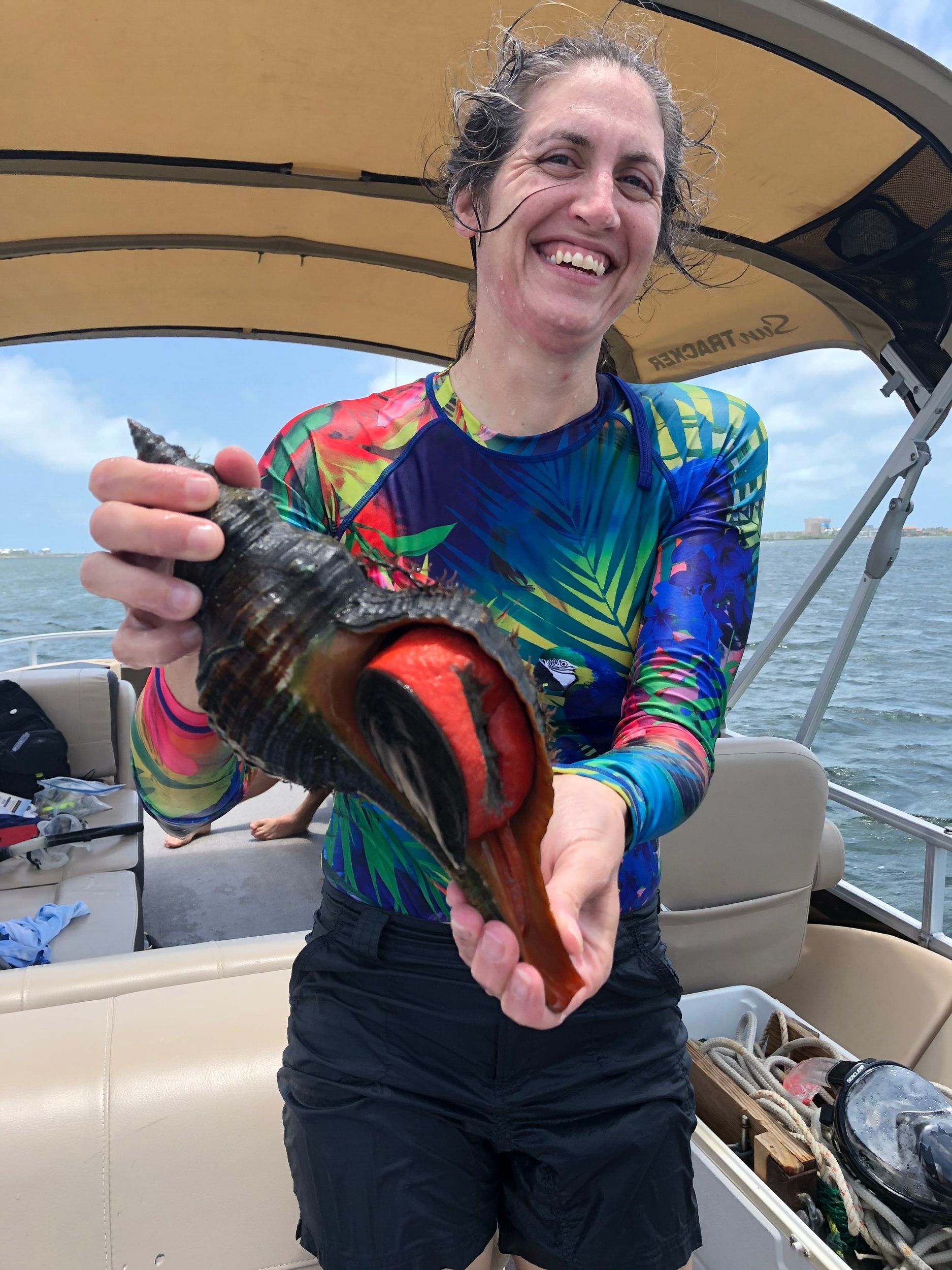 A woman is holding a large sea shell on a boat.