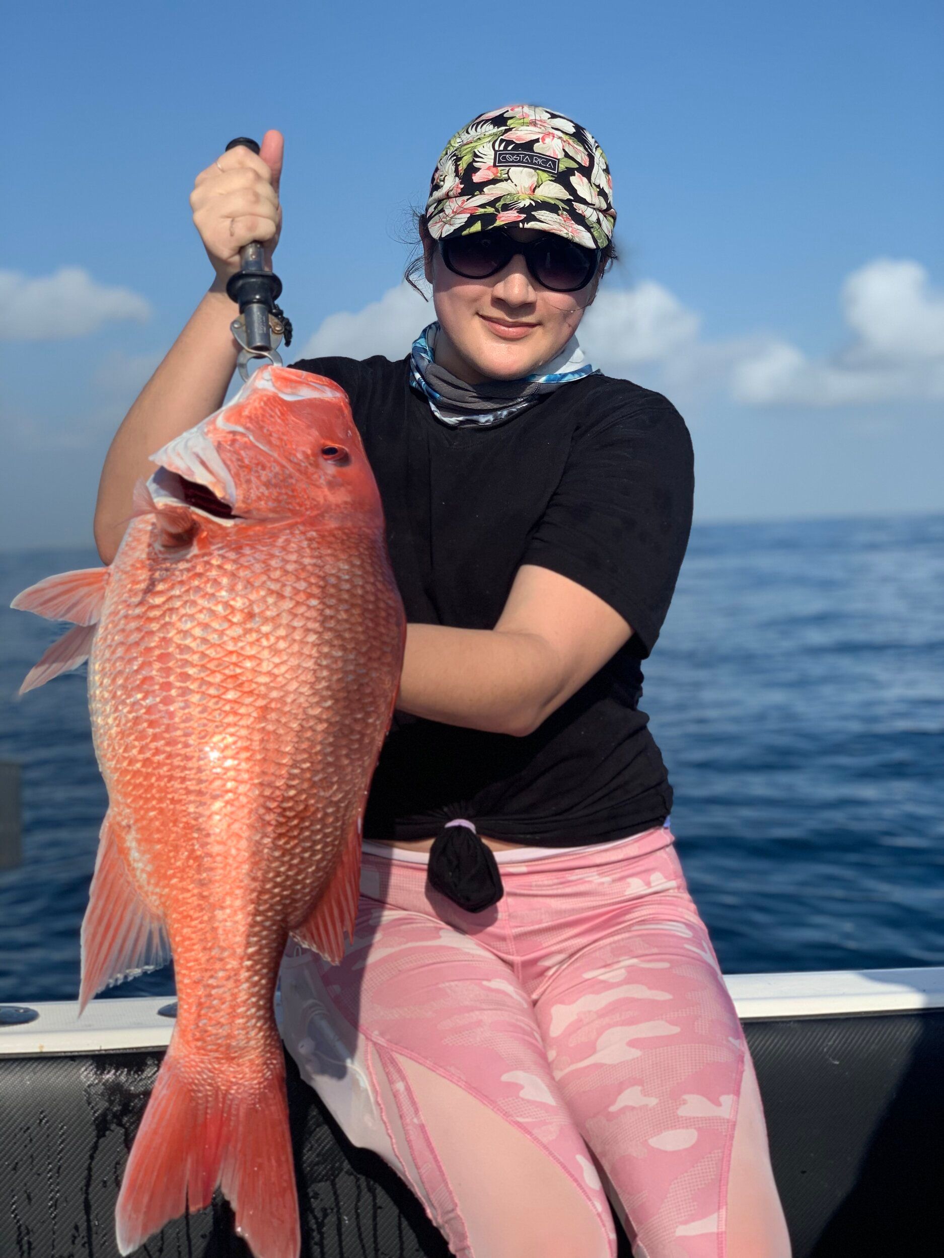 A woman is sitting on a boat holding a large red fish.