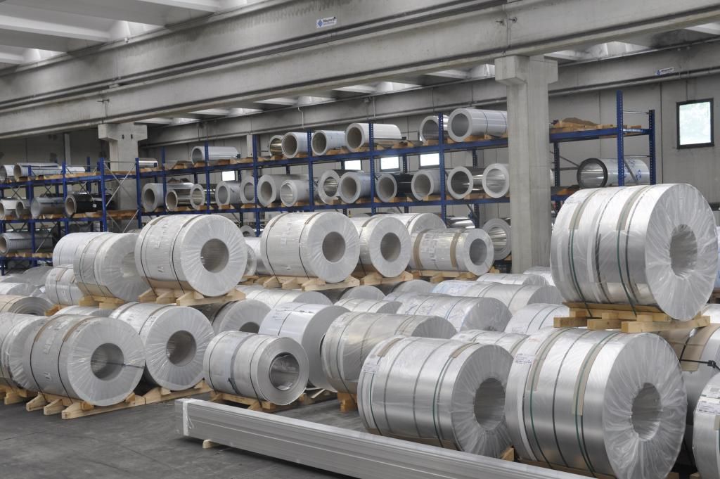 Bobine di metallo impilate su pallet all'interno di un magazzino.