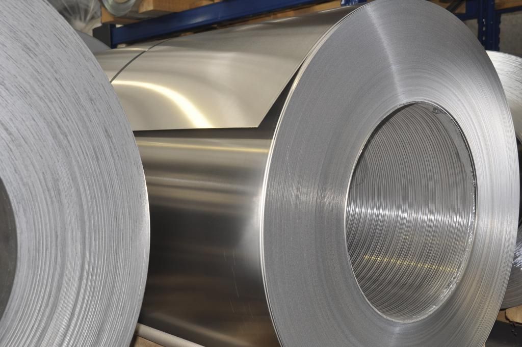 Bobine di metallo argentato e lucido, probabilmente alluminio, accatastate in un'area di stoccaggio.