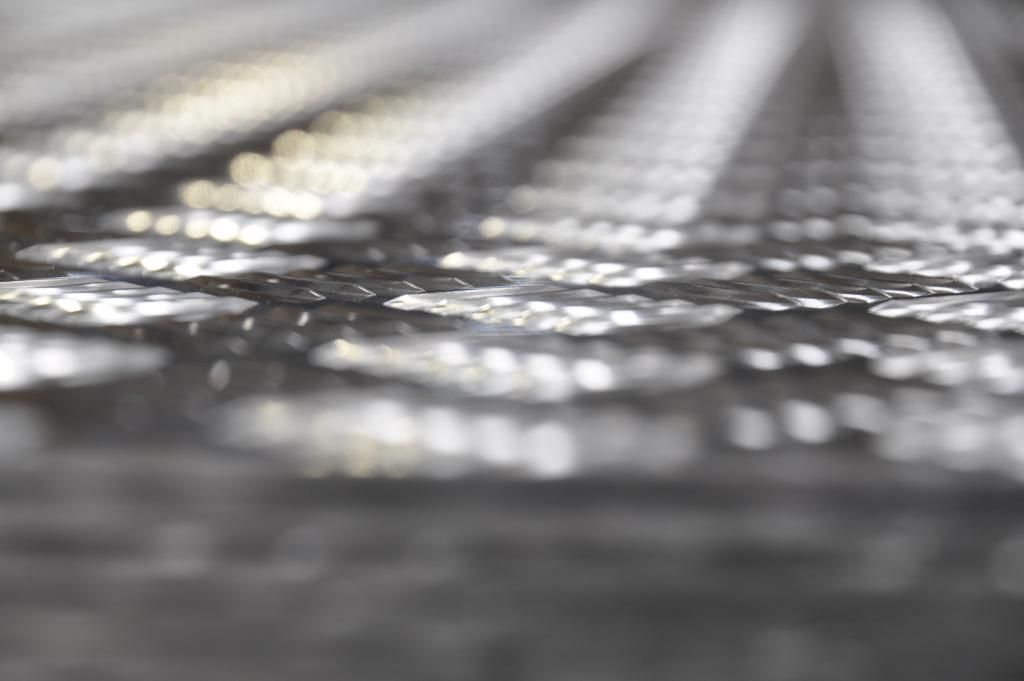 Primo piano di una superficie metallica riflettente e strutturata con un motivo di piccole forme disposte in file.