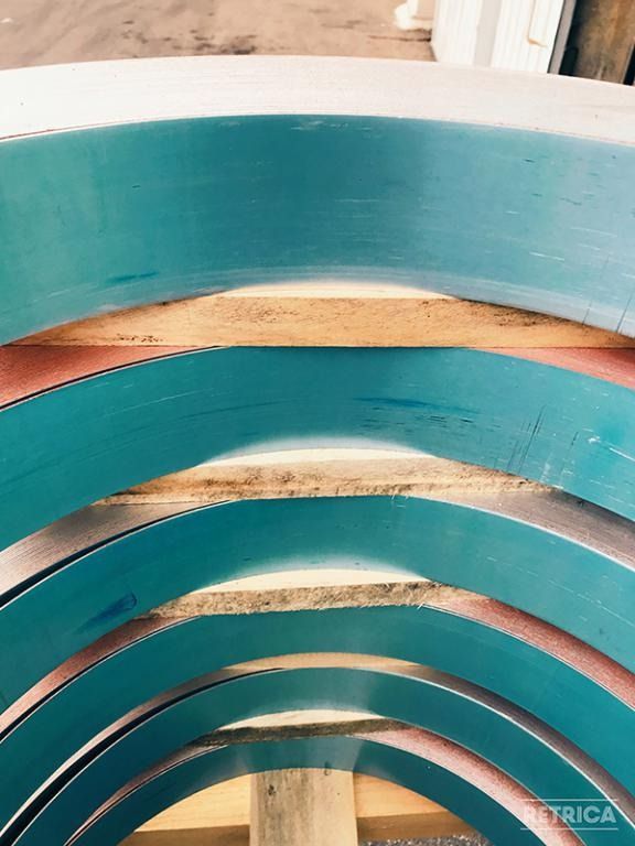 Fasce curve blu sovrapposte con travi di sostegno in legno a vista.