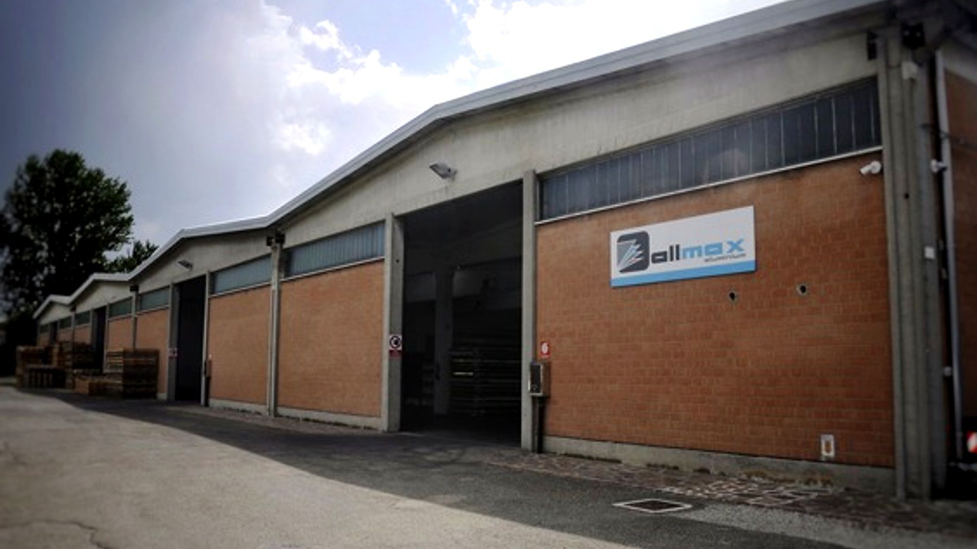 Esterno del magazzino con porta aperta, pareti in mattoni e cartello Dimax.