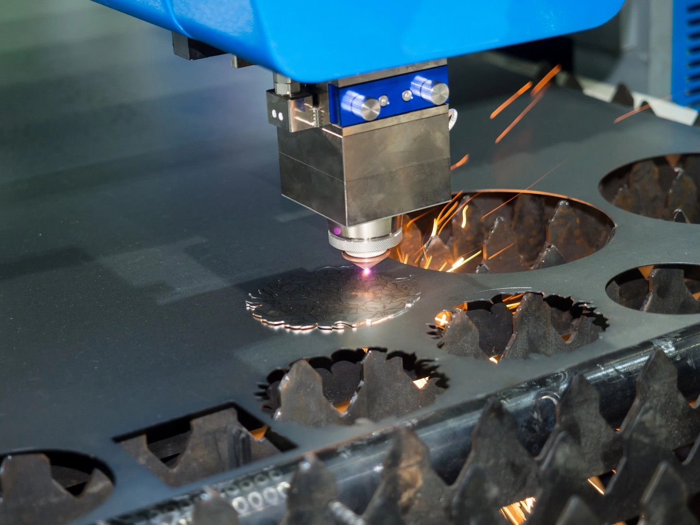 Taglierina laser che taglia forme da una lamiera, scintille che volano, testa della macchina blu.
