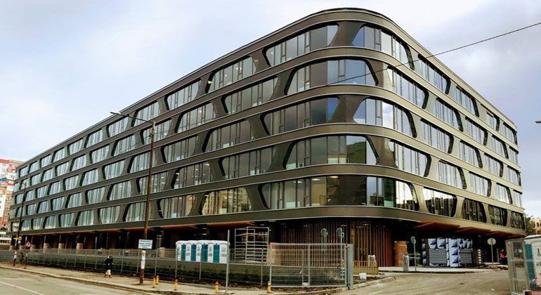Moderno edificio a più piani con facciata scura e bordi curvi.