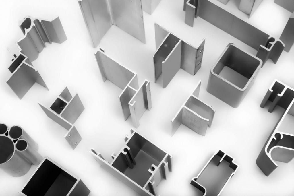 Profili in alluminio assortiti di varie forme e dimensioni, sparsi su una superficie bianca.