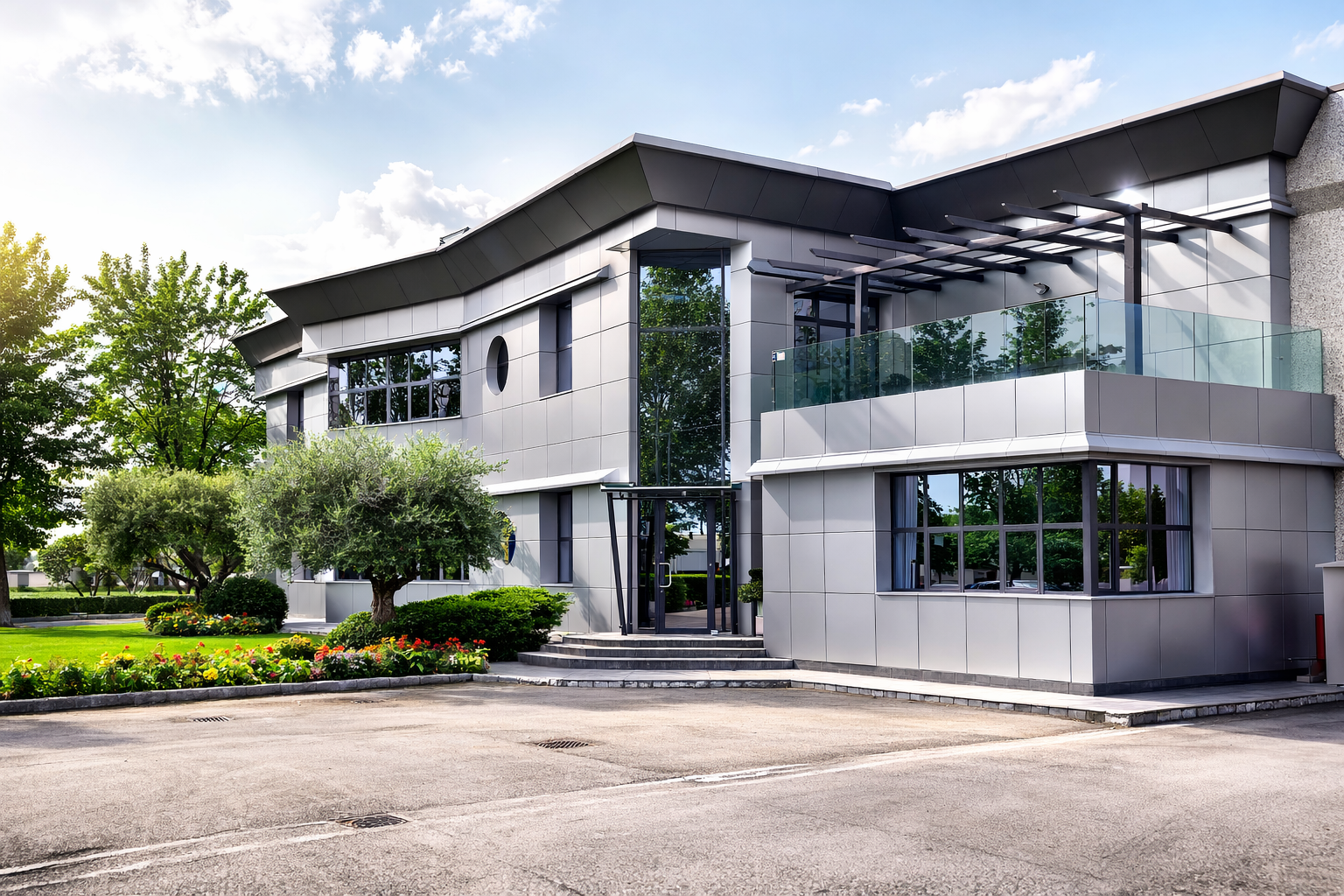 Edificio moderno con facciata metallica, finestre in vetro e balcone. Circondato da alberi e prato verde.