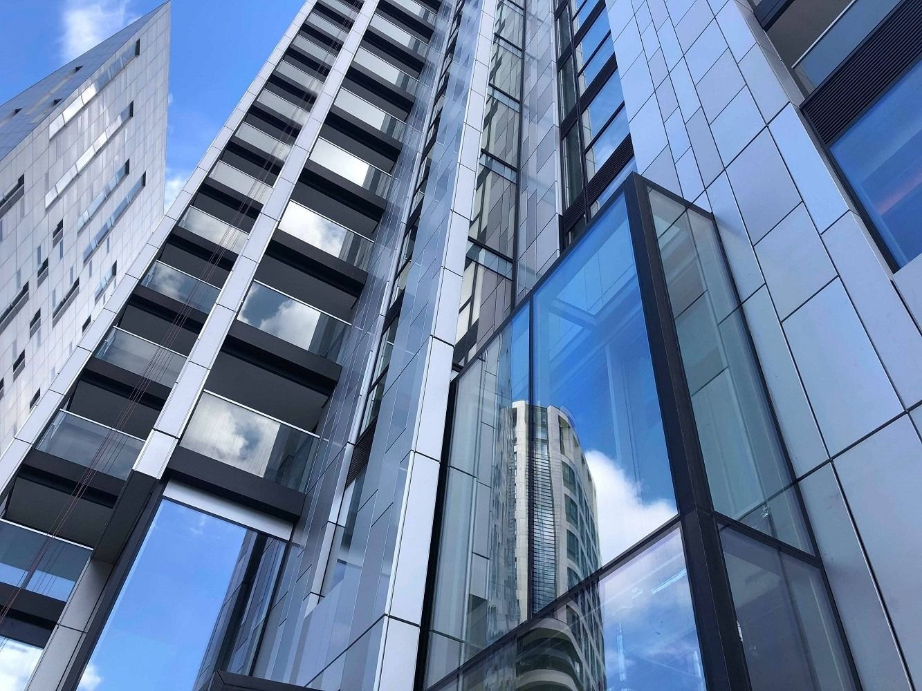 Moderni grattacieli con pannelli in vetro e argento che riflettono il cielo, inclinati verso l'alto.