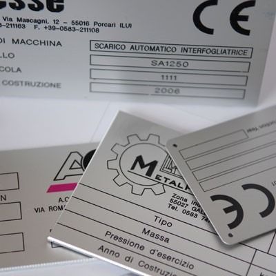 Primo piano di diverse targhette metalliche per macchine con testo stampato, tra cui 