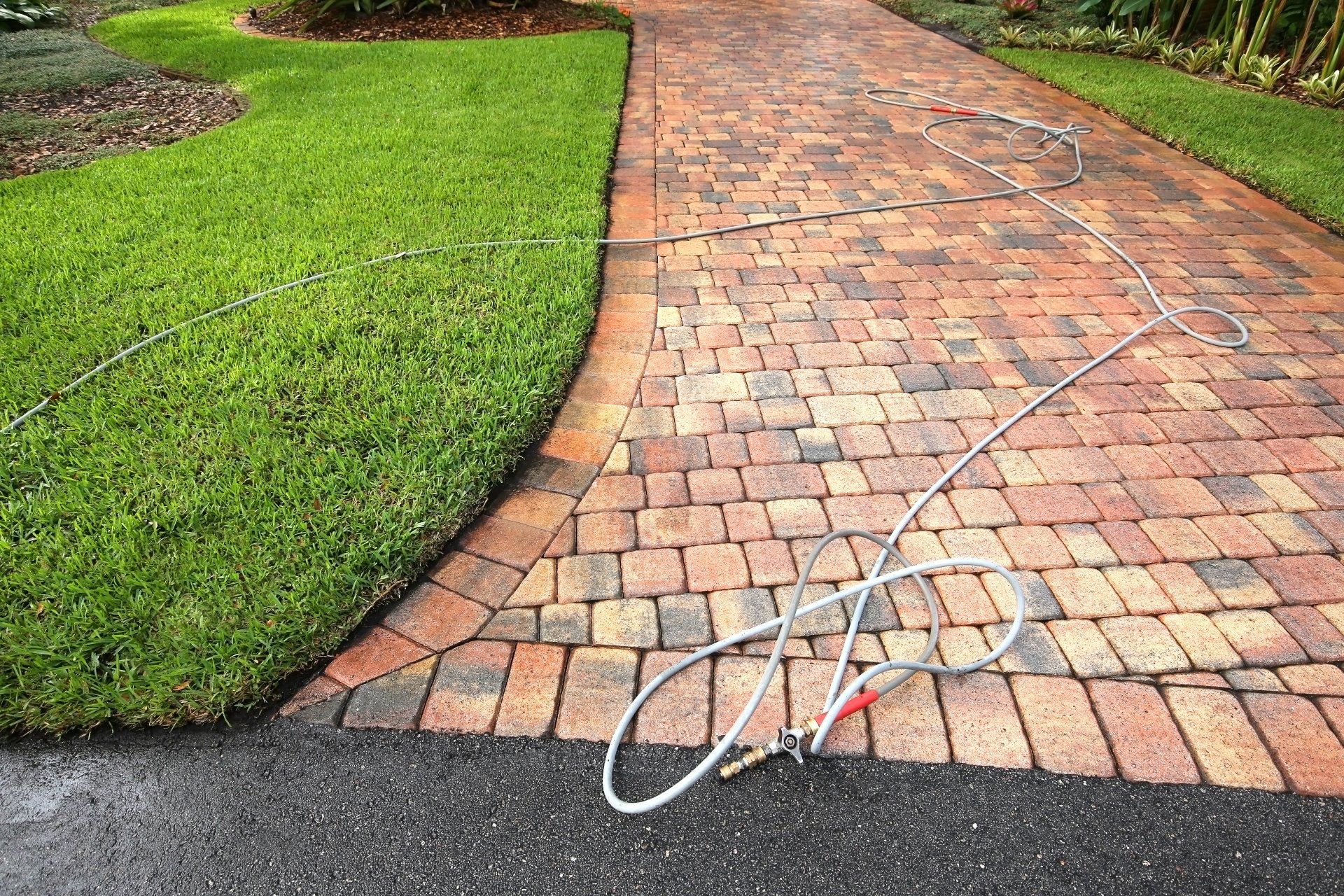 Paver driveway professionally pressure cleaned, with the hose and wand on the driveway