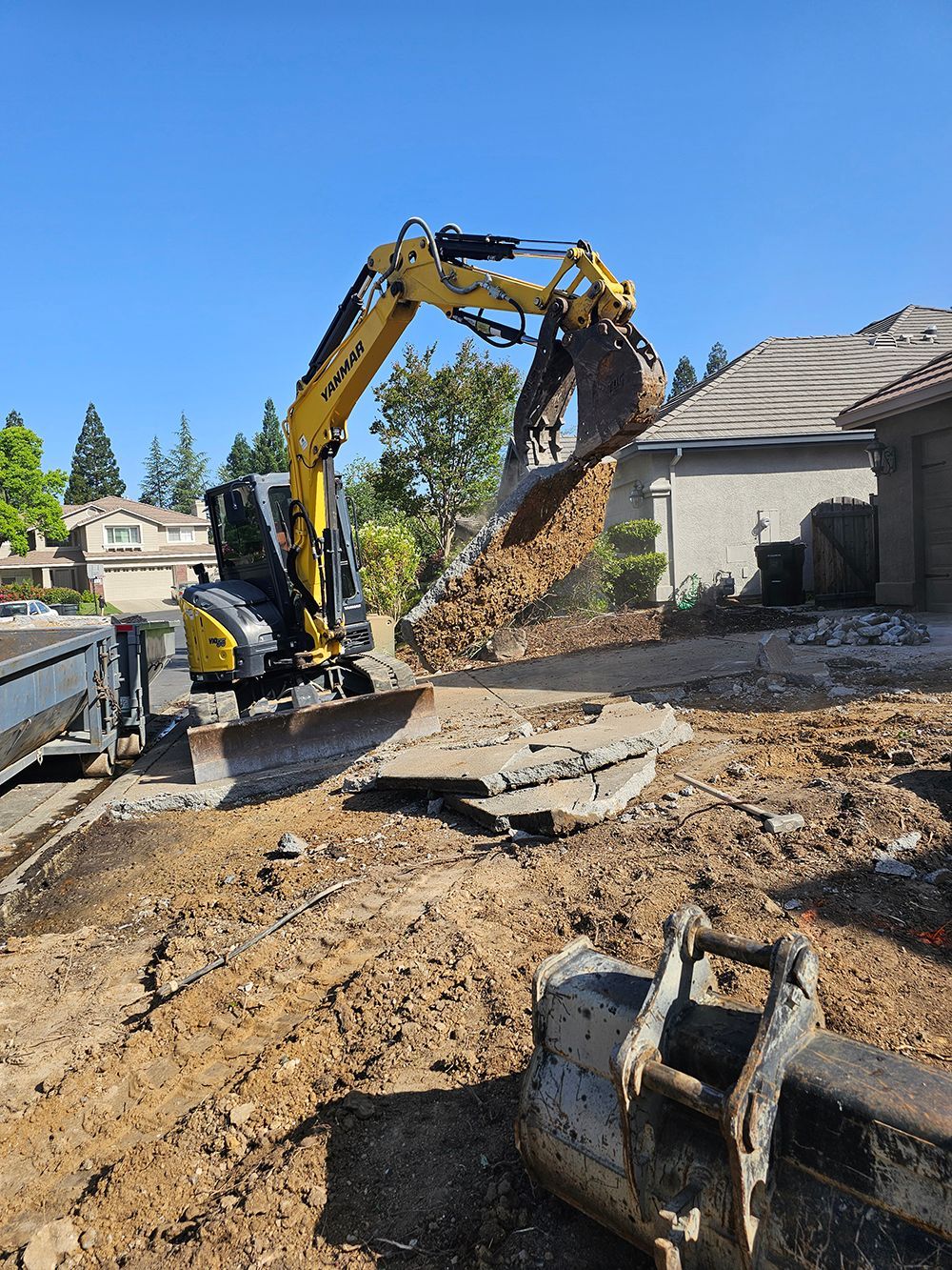 A yellow excavator is digging a hole in the dirt in front of a house.