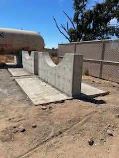 A concrete wall is sitting in the middle of a dirt field next to a fence.