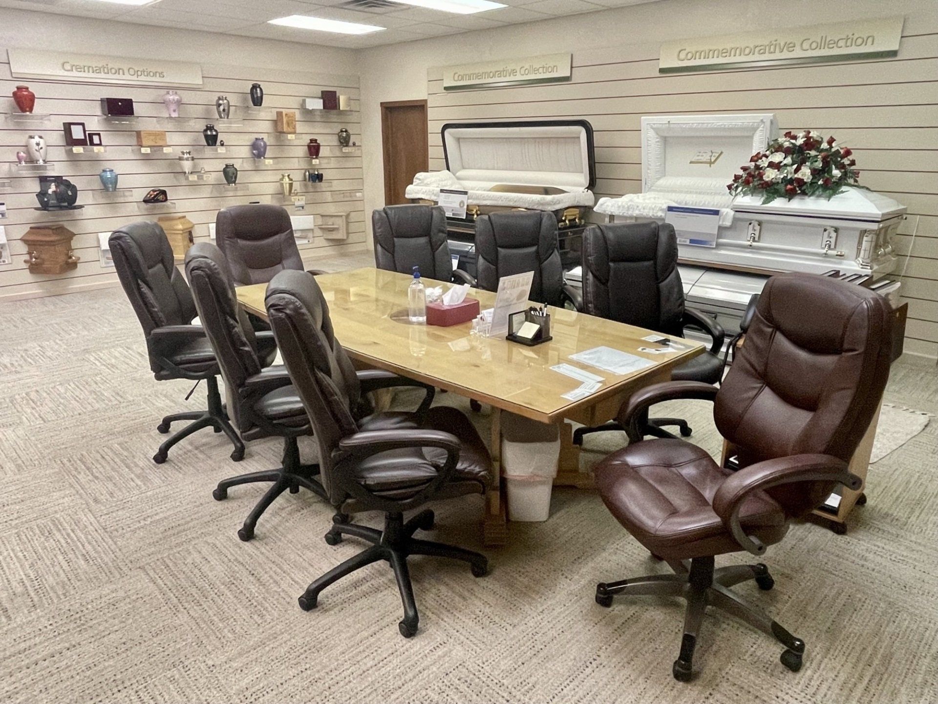 Conference room with a large table, chairs, and caskets on display. Urns are mounted on the wall.